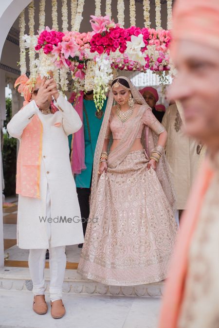 Photo of A bride in a soft pink lehenga entering under a phoolon ki chaadar