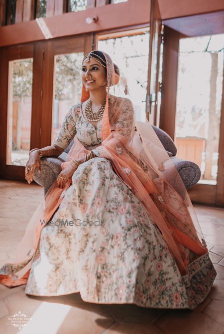 Photo of A bride in a white lehenga with floral embroidery with a peach dupatta