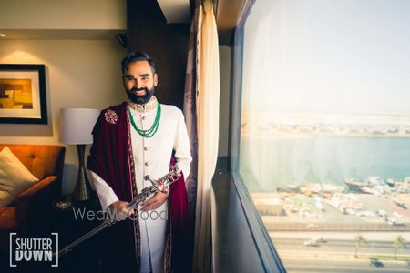 Photo of groom in white sherwani with stole and sword