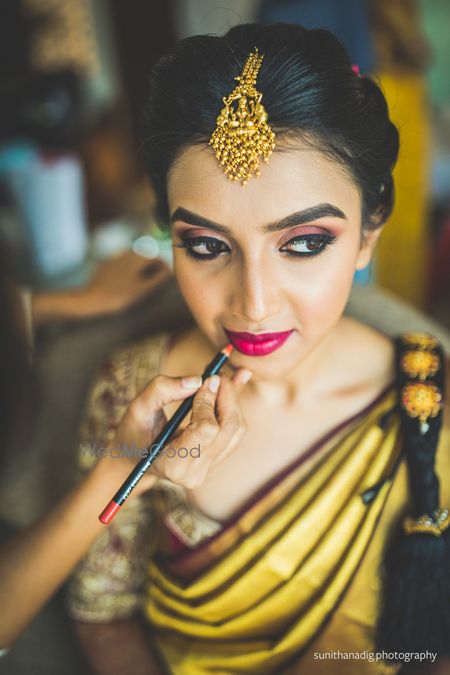 Photo of mua putting bright red lipstick on bride